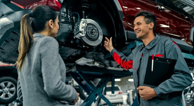 Service_technician_smiling_and_pointing_towards_wheel_brakes_while_talking_to_employee