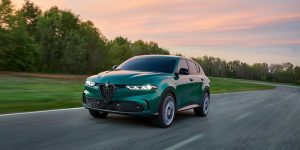 A green 2025 Alfa Romeo Tonale PHEV drives down a road at dusk.
