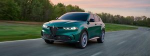 A green 2025 Alfa Romeo Tonale PHEV drives down a road at dusk.