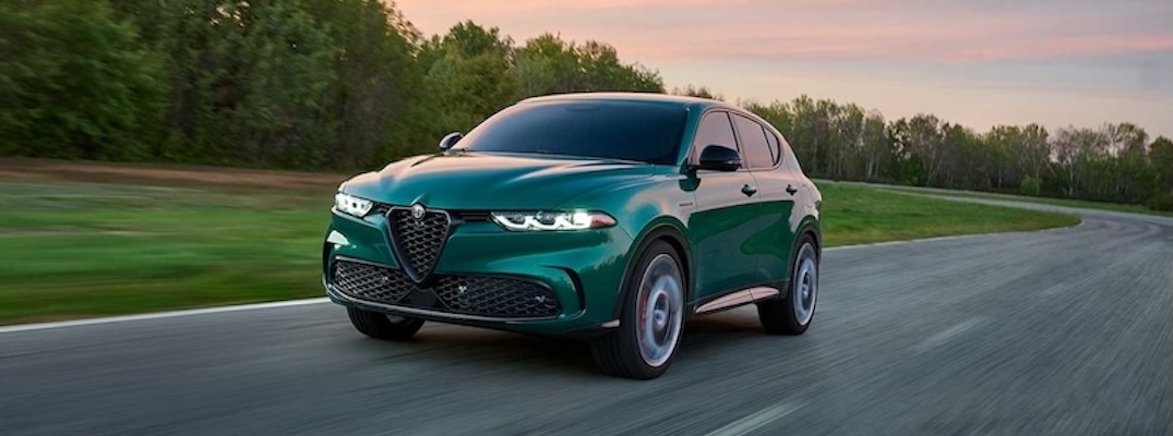 A green 2025 Alfa Romeo Tonale PHEV drives down a road at dusk.