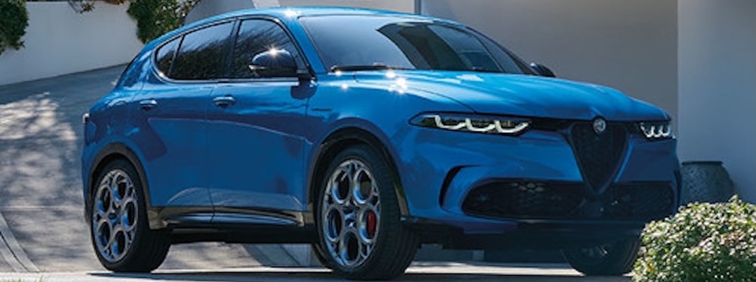 A blue 2025 Alfa Romeo Tonale sits in front of a bush.