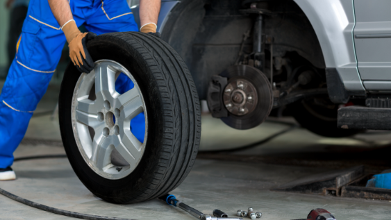 mechanic_rolling_tire_towards_lifted_vehicle_missing_a_tire