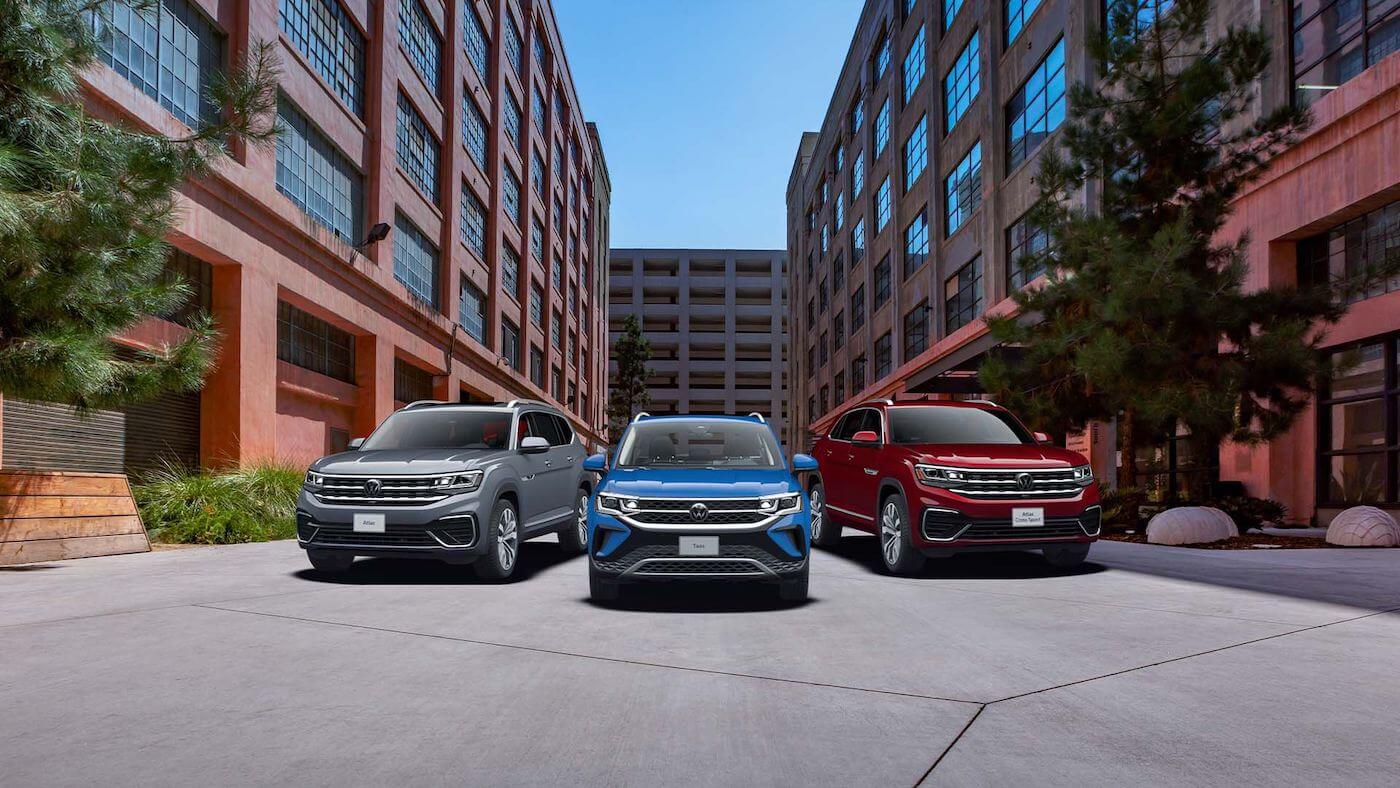 Trois VUS Volkswagen incluant l'Atlas, le Taos et l'Atlas Cross Sport garés entre des bâtiments