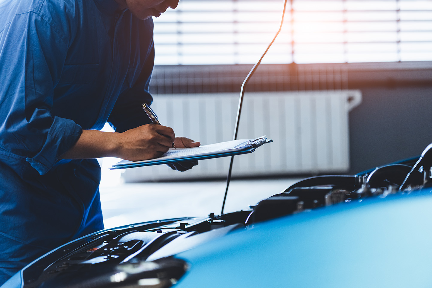 Car mechanic holding clipboard and checking to maintenance vehicle by customer claim order in auto repair shop garage. Engine repair service. People occupation and business job. Automobile technician