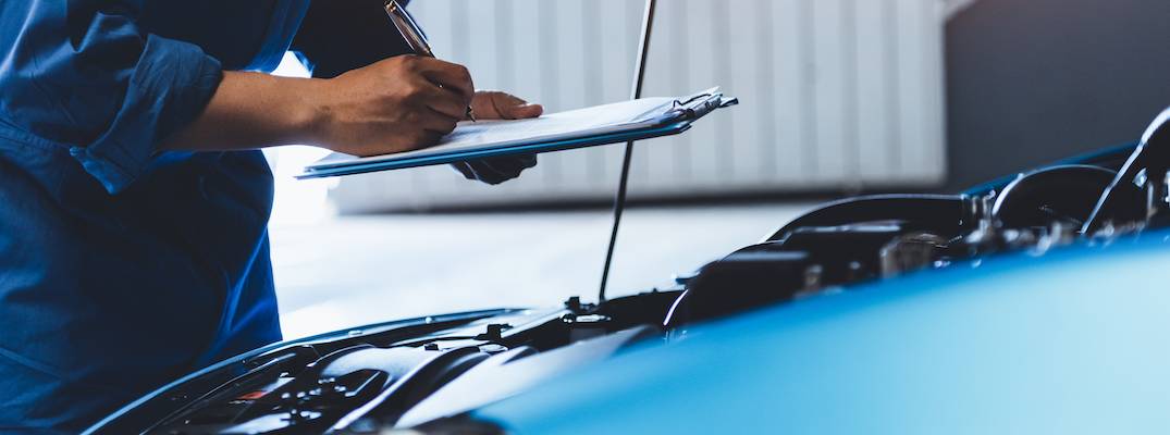 Car mechanic holding clipboard and checking vehicle