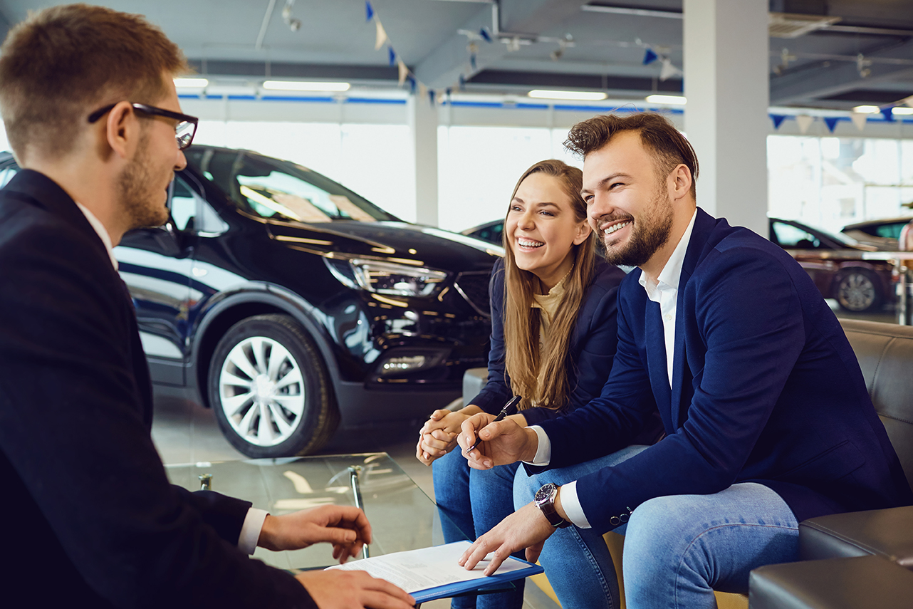 Two people discussing something with a third at a car dealership