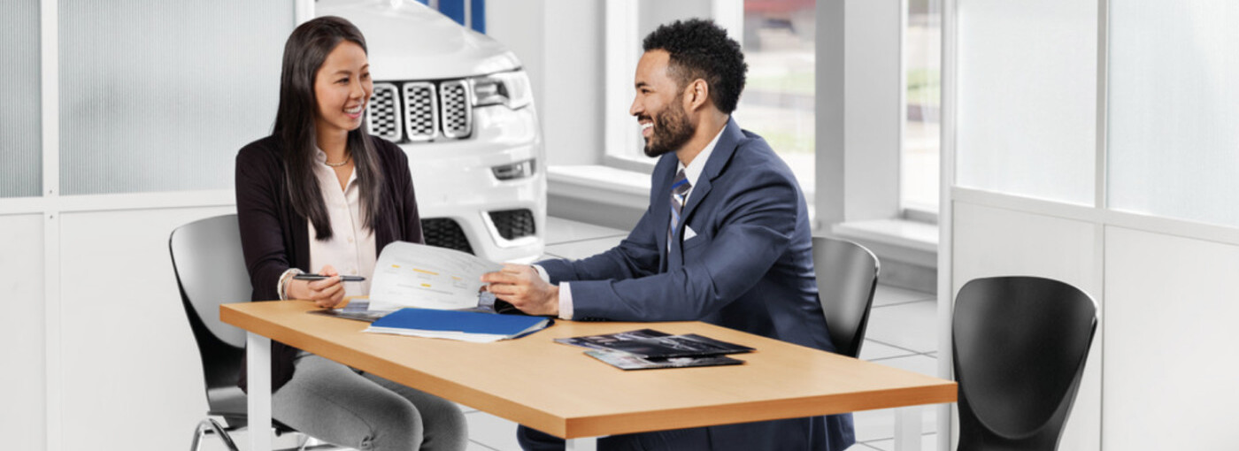 Two people signing paperwork in what appears to be a car dealership