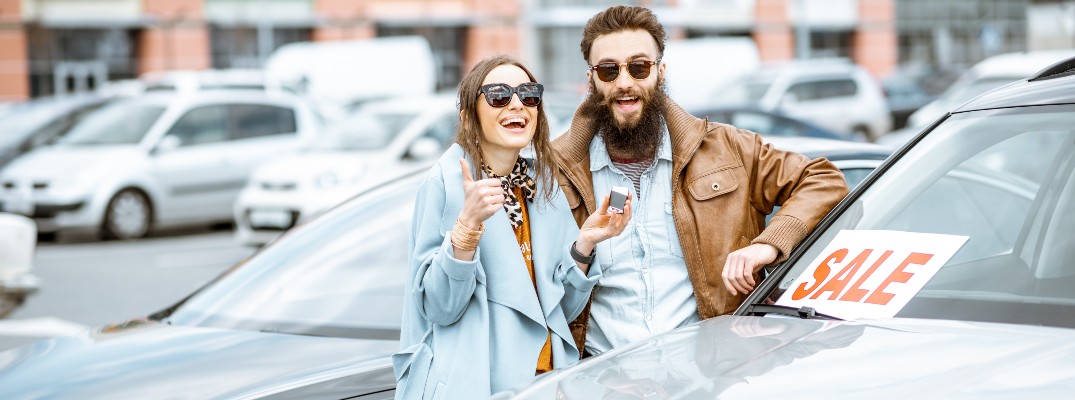 A man and woman standing next to a car for sale