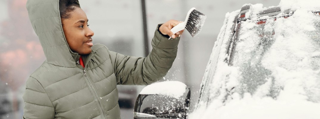 A stock photo of a person brushing snow off their car.