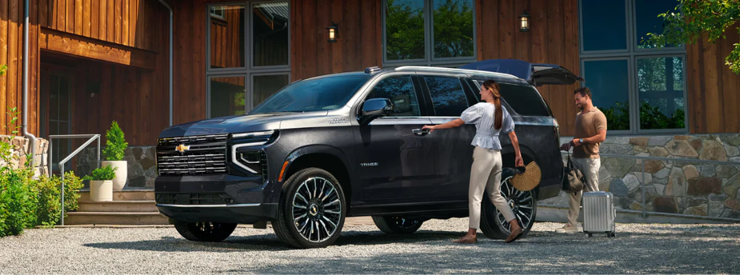A woman opening the door of the 2026 Chevrolet Tahoe while a man packs bags into the trunk