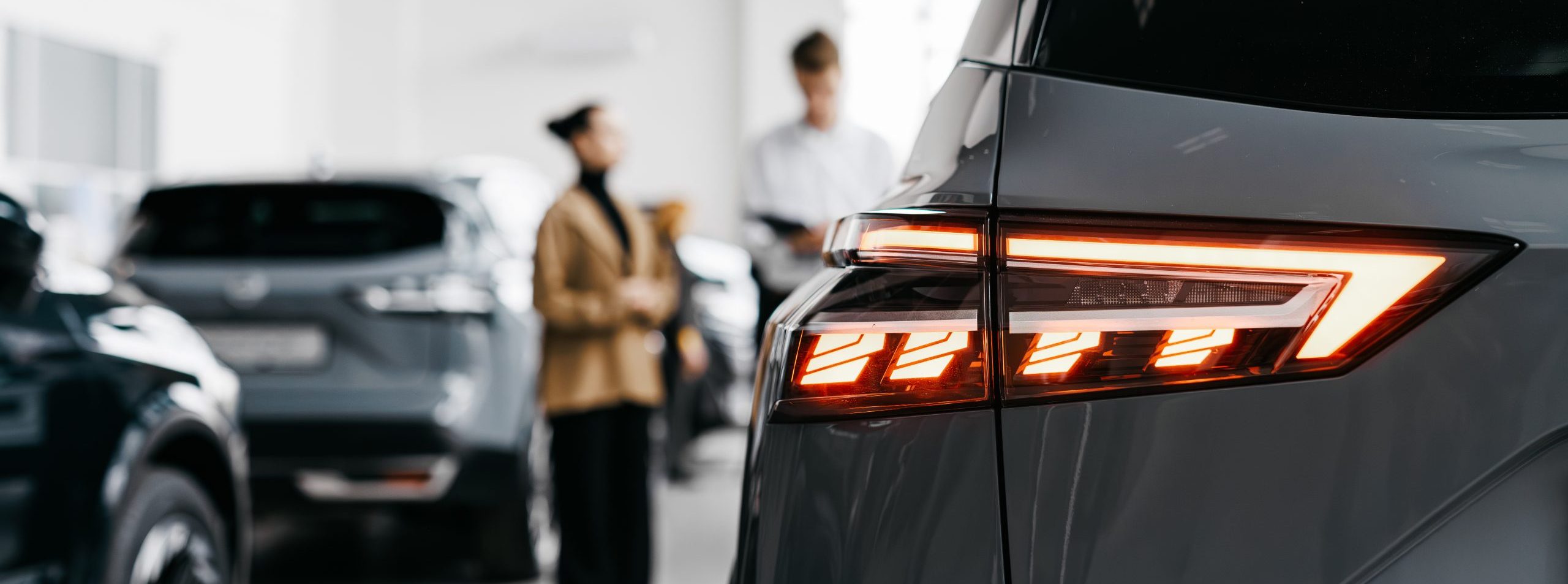 Modern car dealership interior showcasing sleek vehicles with a focus on a gray car's rear lights, highlighting the vibrant atmosphere of automotive sales and customer engagement