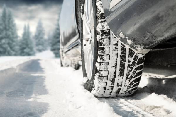 A close up on a car's winter tires, caked with snow as it drives across a white road