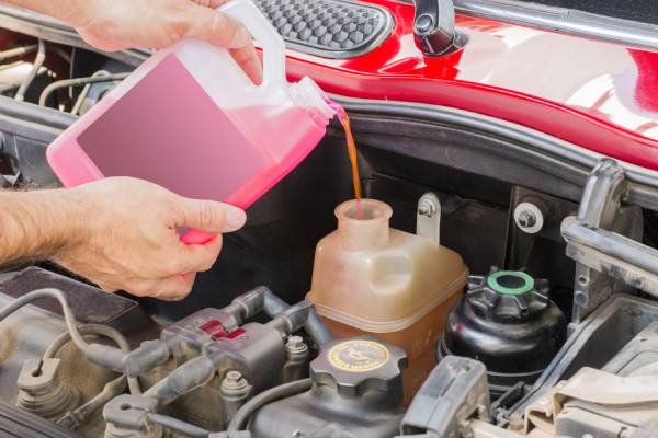 Hands pour pink fluid into a car's reservoir