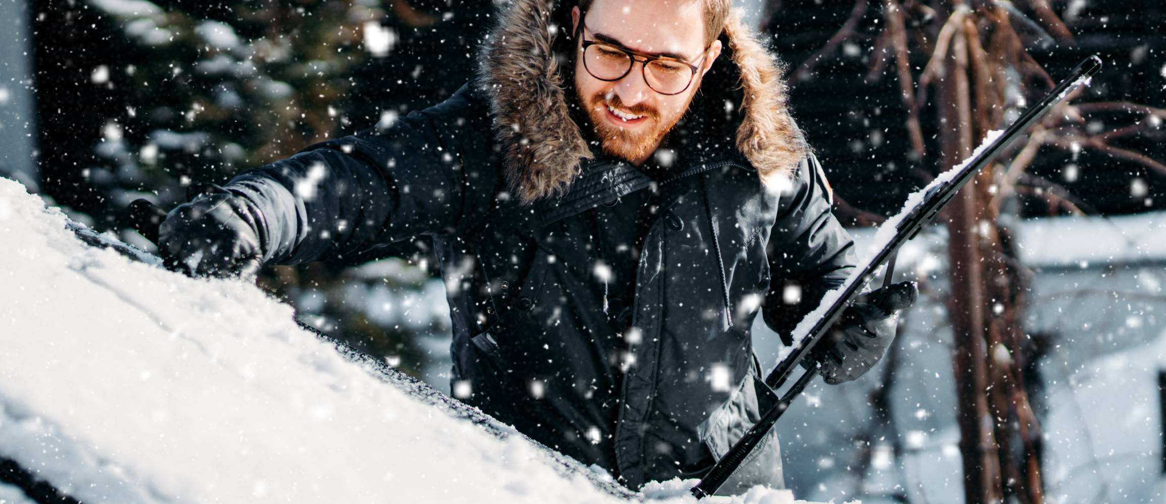 portrait of smiling man cleaning snow off his car during winter snowfall