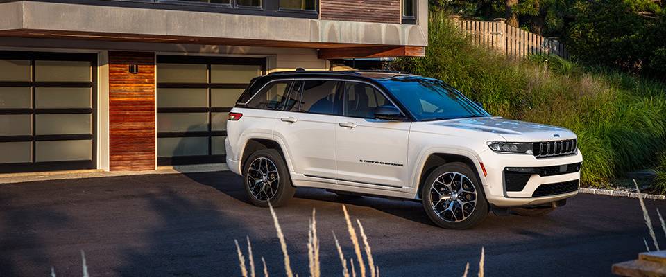 A 2026 Grand Cherokee with a black roof parks outside of a house with wood walls