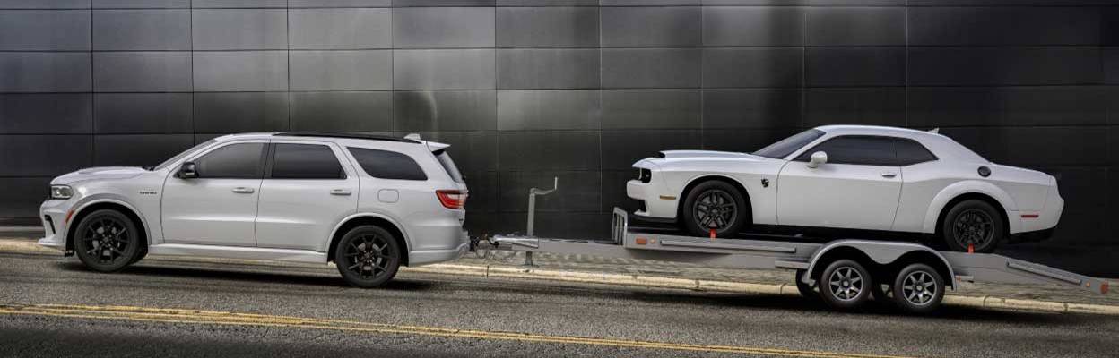 A white 2026 Dodge Durango pulls a trailer carrying a white sedan
