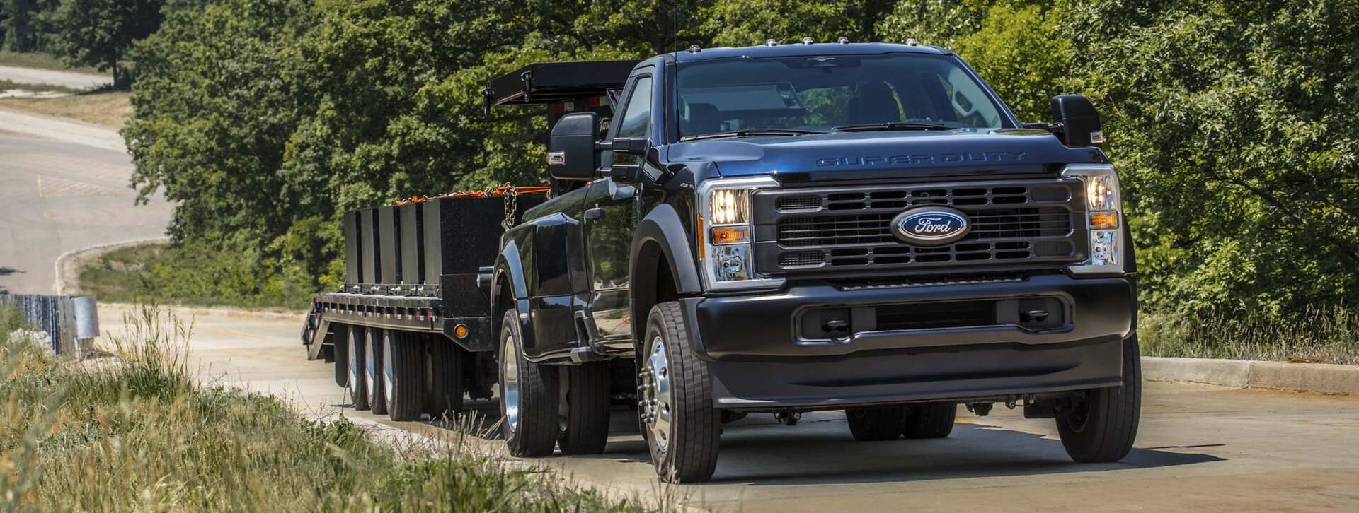 Front side view of 2026 Ford Super Duty hauling trailer with trees in the background