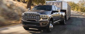 A black 2026 Ram HD pulls a silver trailer. New 2026 Ram 2500 & 3500 Towing and Payload Guide at Blenheim Chrysler Dodge Jeep Ram in Blenheim, ON