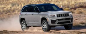 A silver 2026 Jeep Grand Cherokee drives across off-road terrain. New 2026 Jeep Grand Cherokee performance & engine guide at Blenheim Chrysler Dodge Jeep Ram in Blenheim, ON