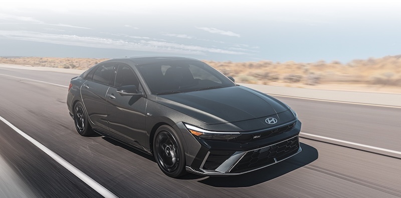 Exterior shot of a black 2025 Hyundai Elantra driving by the waterfront.