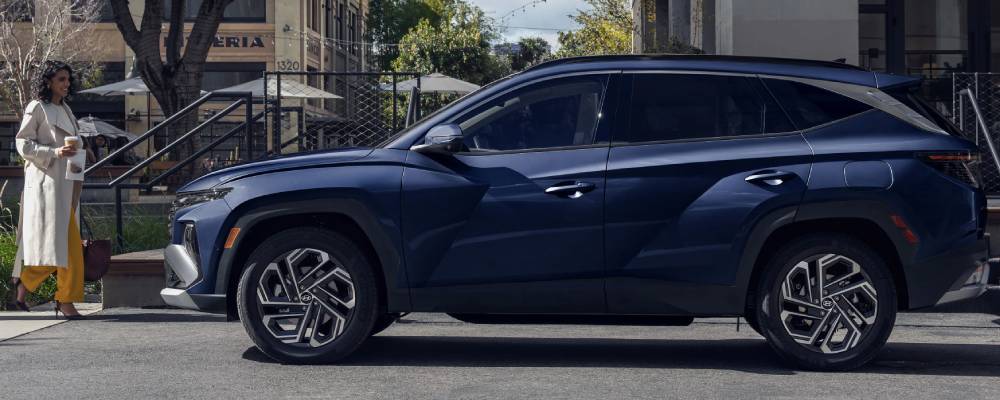 A dark blue 2026 Hyundai Tucson is parked outside an apartment. A woman walks towards it. 2026 Hyundai Tucson vs. 2026 Nissan Rogue vehicle comparison at Calgary Hyundai in Calgary, AB