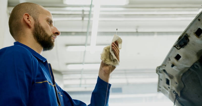 A mechanic looks at the engine oil dipstick on a vehicle.