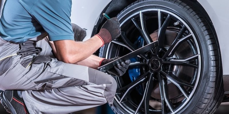 A mechanic checks a tire on a silver car.