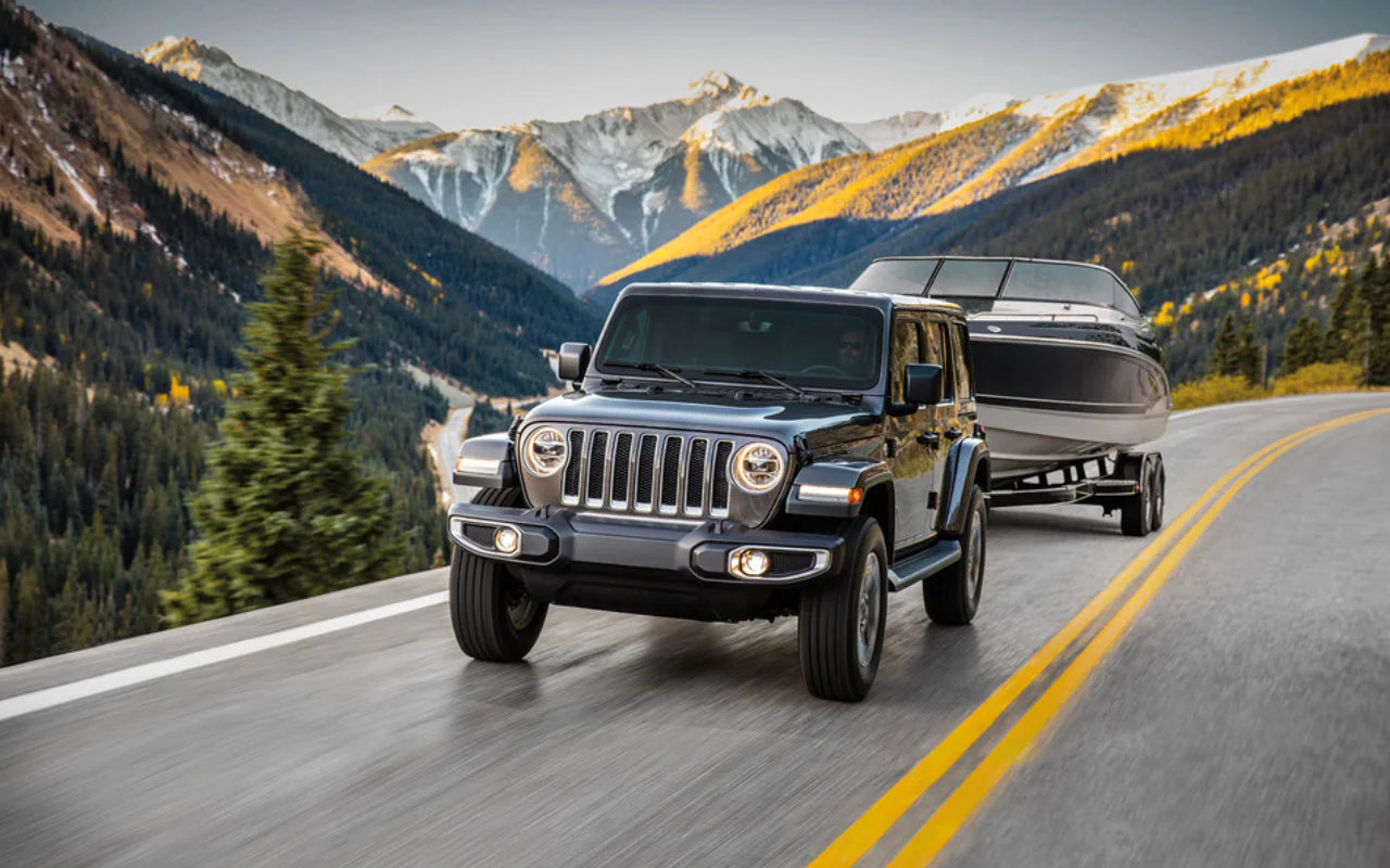 vue latérale avant d'un Jeep Wrangler 2023 remorquant un bateau sur une route de montagnes