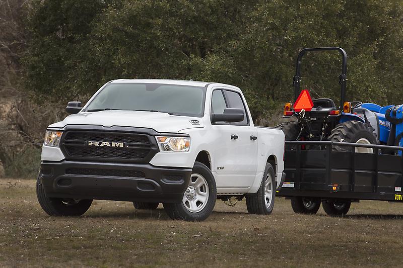 Vue 3/4 avant d'un RAM 1500 Tradesman blanc remorquant un tracteur dans un champs