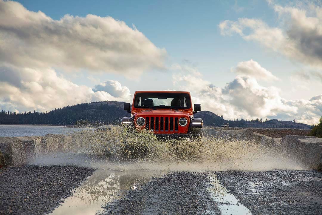 Vue avant d'un Jeep Wrangler Rubicon 2021 éclaboussant l'eau en roulant sur un chemin bouetteux