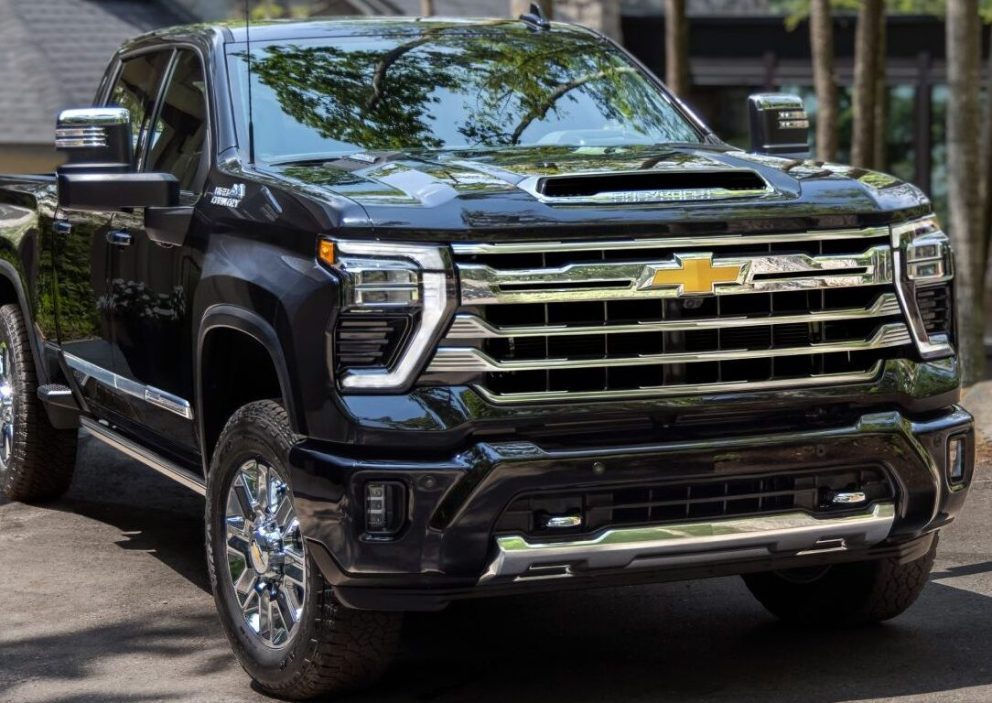 A black 2025 Chevrolet Silverado HD parks outside of a cabin in the woods