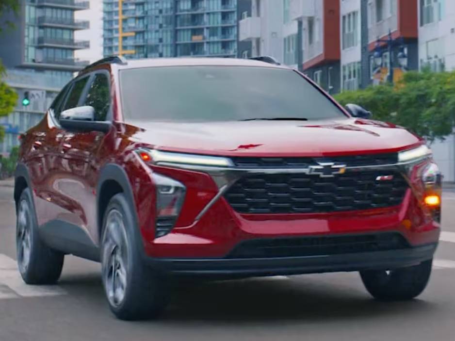 A red 2025 Chevrolet Trax drives through a city with its lights on