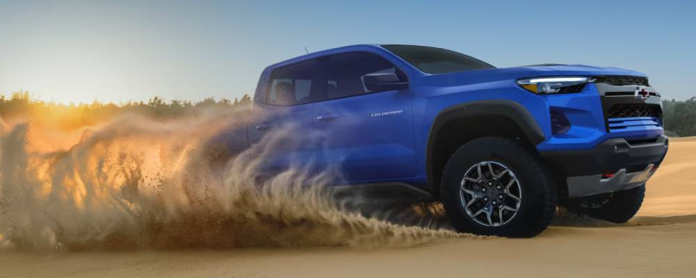 A blue 2026 Chevrolet Colorado drives across the desert, kicking up sand. New 2026 Chevrolet Colorado towing and performance specs at College Park GM in Vermilion, AB
