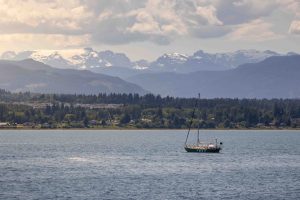 sailboat in the ocean with mountains in the background in the comox valley