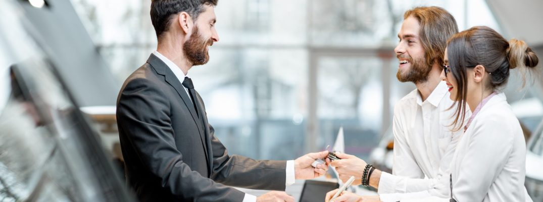 A couple talks with a sales rep at a dealership to buy a vehicle.