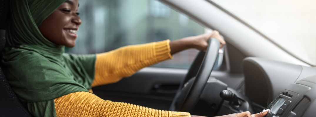 Positive black religious lady in hijab listening radio in car, changing channels