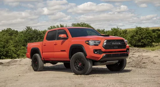 Orange Toyota Tacoma pickup truck parked outdoors on rugged terrain, featured by Driven Auto Group Newmarket.