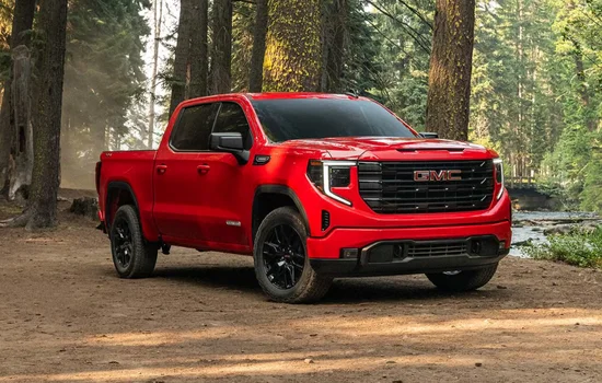 Red GMC Sierra 1500 pickup truck parked in a forest setting, showcasing rugged design and refined strength at Driven Auto Group Newmarket.
