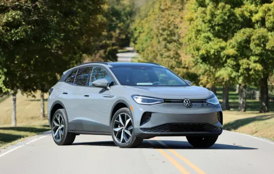 White Volkswagen ID.4 AWD (2021+) electric SUV driving on a tree-lined road, featured by DRIVEN Newmarket.