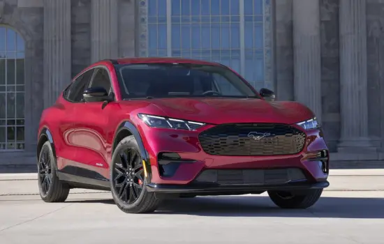 Red Ford Mustang Mach-E AWD (2021+) electric SUV parked in front of a modern building, featured by DRIVEN Newmarket.