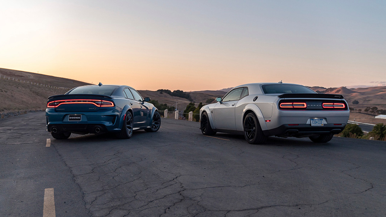 rear side view of two  2023 Dodge Chargers on a country road at sunset