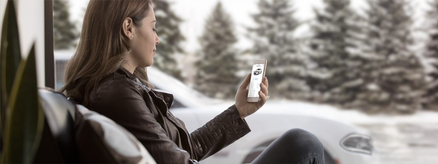 view of a woman in her living room, browsing the uconnect 5 app on her smartphone