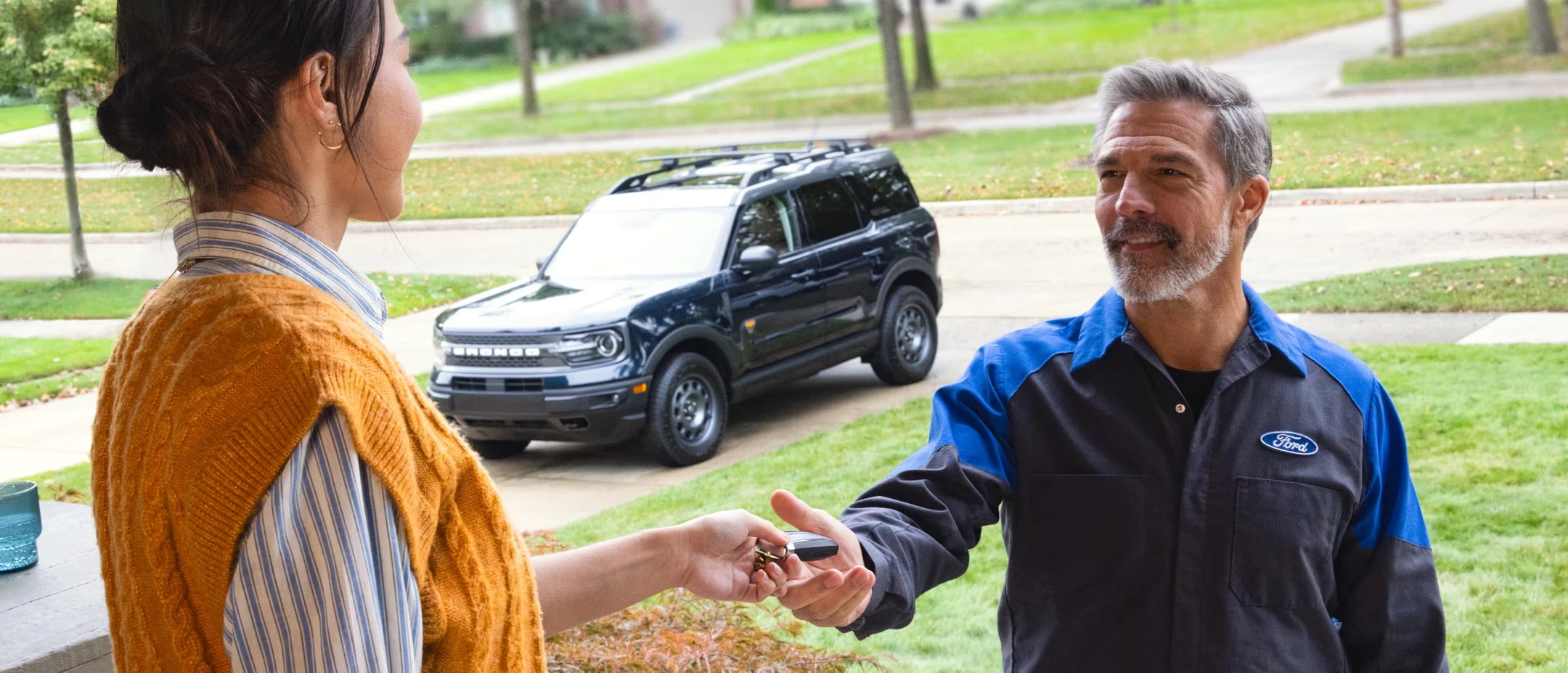 Ford employee handing unknown person a key outdoors, Ford Bronco parked in driveway