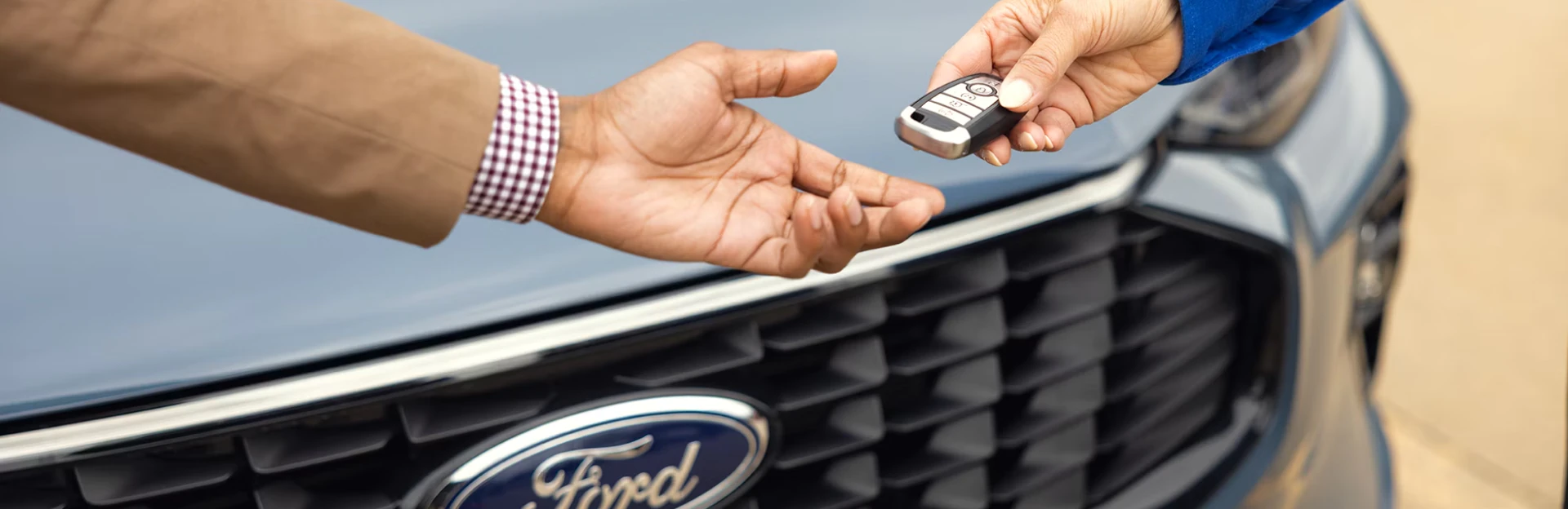 Unknown person handing another person a key as they stand in front of a Ford vehicle