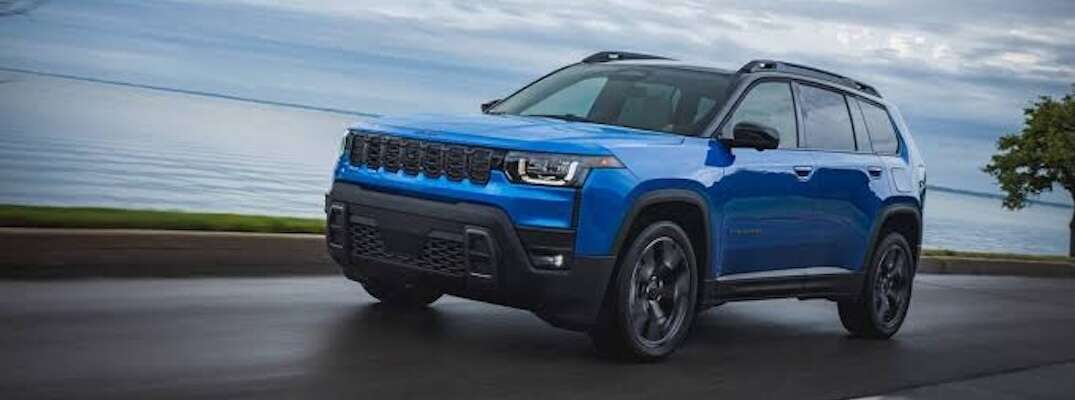 A blue 2026 Jeep Cherokee drives by a lake.