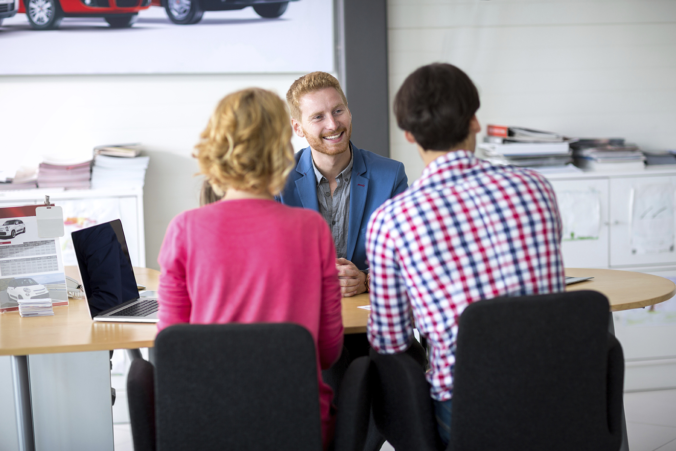 Couple negotiating sale contract for car, back view