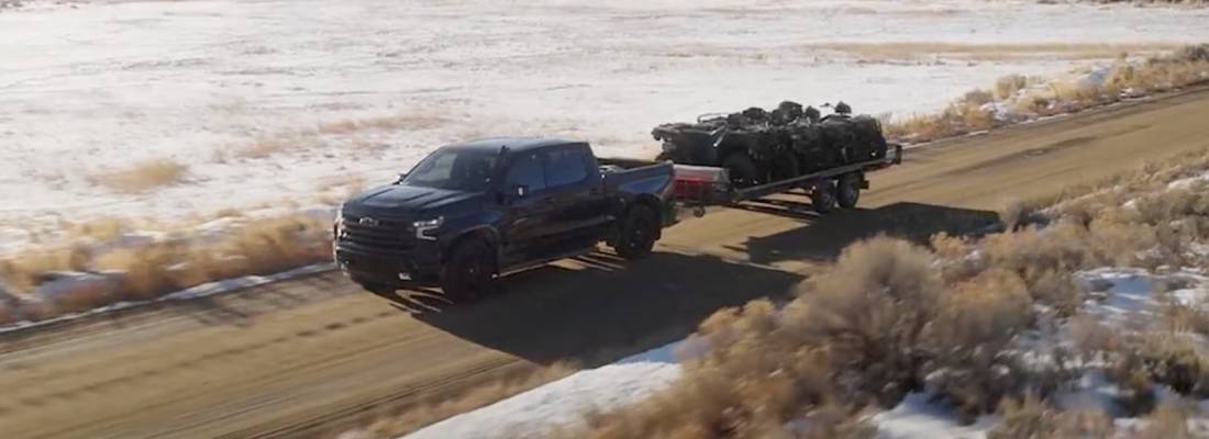 A black 2026 Chevrolet Silverado 1500 pulls a trailer along a dirt track road