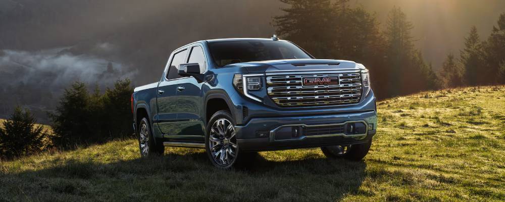 A blue 2026 GMC Sierra 1500 drives up a grassy hill