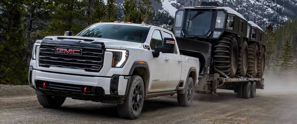 A white 2026 Sierra HD pulling a trailer loaded with vehicles. New 2026 GMC Sierra HD towing and engine specs at Gardner GM in Hope, BC