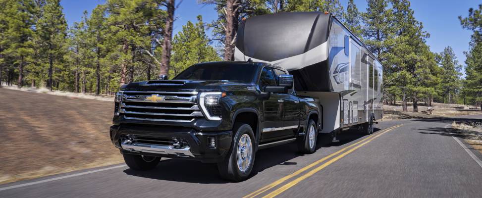A black 2026 Chevrolet Silverado HD pulls a full size black and silver travel trailer. New 2026 Chevrolet Silverado 2500 & 3500 HD engine and towing specs at Gardner GM in Hope, BC